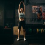 Strong woman stretching her arms in an industrial-style gym environment with motivational wall art.